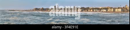 Vue panoramique de la côte de Swakopmund en Namibie au coucher du soleil, regardant à travers les vagues de l'Atlantique vers la ville historique du front de mer. Banque D'Images