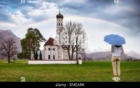 Une touriste avec un parapluie se tient devant la belle église Saint-Coloman à Schwangau, Allgäu, en Allemagne, par un jour de pluie Banque D'Images