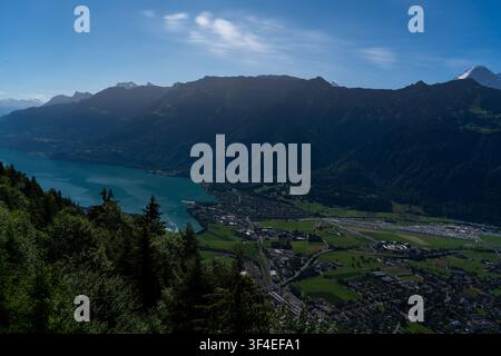 Vue du Harder Kulm sur la ville d'Unterseen, les eaux turquoise du lac de Thoune et les Alpes bernoises dramatiques sous un ciel bleu clair à Unte Banque D'Images