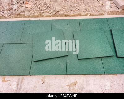 Vue rapprochée de carreaux de revêtement de sécurité posés pour l'installation sur un chantier de construction avec du sable et du gravier à proximité Banque D'Images