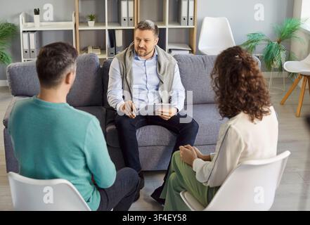 Jeune couple assis sur des chaises et écoutant un psychologue en séance de thérapie. Banque D'Images