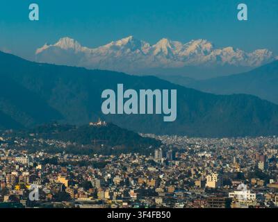 Vue aérienne de la stupa de Swayambhunath perchée sur une colline surplombant l'étalement urbain dense de Kathmandu avec la chaîne de montagnes enneigée de l'Himalaya Banque D'Images