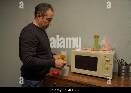 Homme préparant du café instantané dans une tasse à côté d'un four à micro-ondes sur une commode en bois Banque D'Images