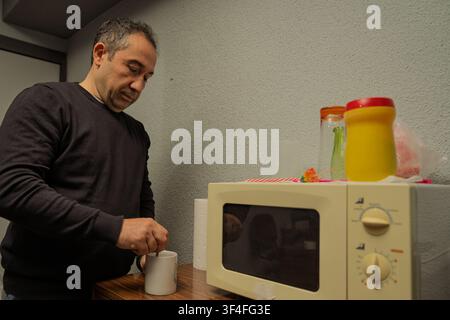 Homme remuant une boisson chaude dans une tasse à côté d'un four à micro-ondes Banque D'Images