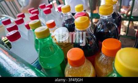 Bouteilles en plastique variées contenant différentes boissons sucrées rafraîchissantes avec des bouchons colorés, positionnées pour la vente ou la rafraîchissement par une journée ensoleillée Banque D'Images