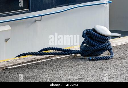 Corde tressée bleue enroulée autour d'un bittement en métal dans une marina, illustrant le travail maritime et les responsabilités du quai. Banque D'Images