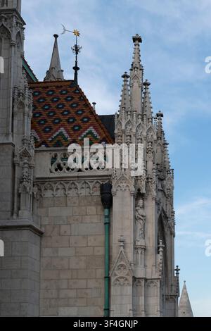 Des flèches gothiques en pierre élancées ornées de feuillage sculpté s'élèvent au-dessus d'un toit carrelé Zsolnay à motifs de diamants sur le bâtiment du ministère de l'Intérieur Banque D'Images