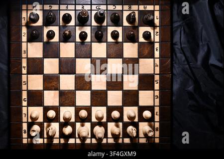 Vue en plongée d'un échiquier en bois avec toutes les pièces disposées en position de départ. Le contraste dramatique entre les nuances claires et sombres avec des ombres subtiles symbolise la planification stratégique, la concurrence commerciale, la vision tactique, la prise de décision et le défi intellectuel. Banque D'Images