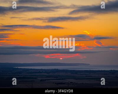 Couchant ardent brille à travers les nuages superposés au-dessus des terres agricoles rurales et d'une côte lointaine du Sussex ; idéal pour les publicités de voyage, de nature, de climat et de campagne Banque D'Images