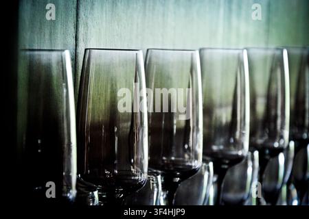 Range d’élégants verres à vin en cristal reflétant une lumière atmosphérique sur un fond texturé sombre, prise artistique avec faible profondeur de champ. Banque D'Images