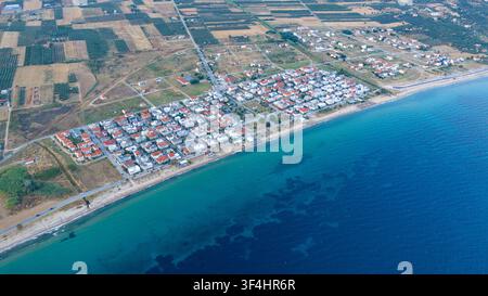 Vue élevée d'une colonie côtière compacte, d'une plage étroite et d'une eau bleu clair bordée par des champs cultivés à Paralia Dionisiou, en Grèce. Banque D'Images