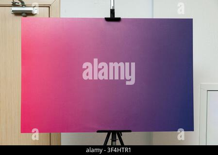 Un grand tableau artistique présentant un dégradé fluide qui passe du rose à gauche au violet à droite est affiché sur un trépied. Le fond Banque D'Images