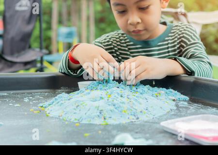 Enfant mignon asiatique jouant avec une pelle en plastique dans un bac à sable de couleur bleue sur un terrain de jeu extérieur. Mise au point sélective. Concept de jeu et d'apprentissage pour les enfants. Banque D'Images