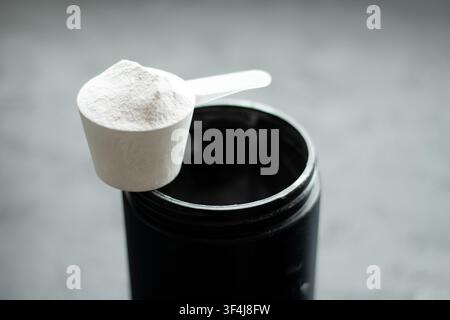 Poudre blanche dans une cuillère doseur positionnée au-dessus d'un récipient noir sur une surface texturée, mettant en valeur une composition propre et minimaliste Banque D'Images