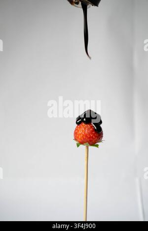Fraise fraîche sur un brochette en bois recouverte de chocolat noir dégoulinant sur un fond blanc. Banque D'Images