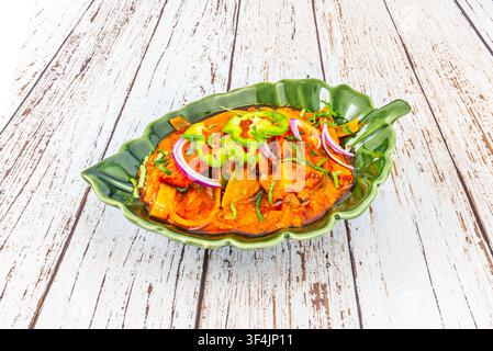 Poulet jalfrezi épicé avec poivrons et rondelles d'oignon rouge, servi dans un plat vert en forme de feuille sur du bois blanchi. Banque D'Images