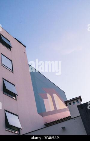 Funchal, Madère. 6 mars 2026. Vue en contre-plongée d'un bâtiment résidentiel moderne présentant une grande fresque géométrique dans des tons rose pastel et bleu contre Banque D'Images