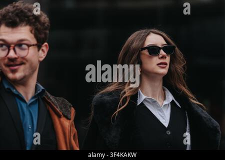 Femme d'affaires élégante en lunettes de soleil marchant avec assurance avec un collègue dans une rue de la ville Banque D'Images