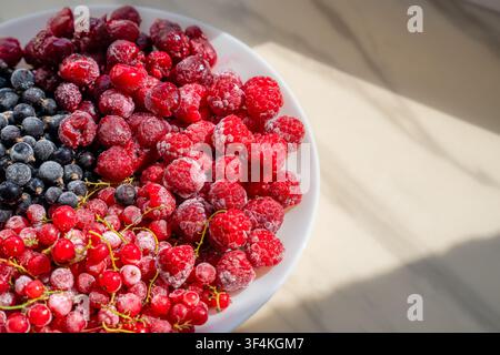 Assiette blanche remplie de framboises congelées, de cassis, de cerises et de groseilles rouges au soleil Banque D'Images