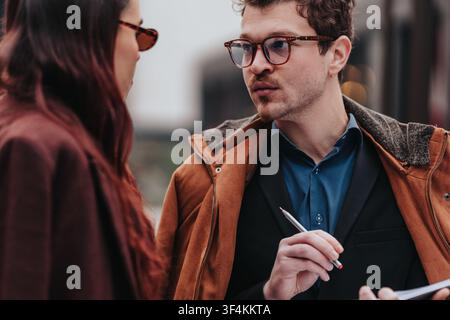 Des collègues d'affaires ayant une conversation concentrée en plein air tout en prenant des notes et en discutant du travail Banque D'Images