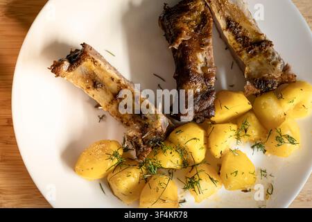 Côtes rôties avec pommes de terre et aneth servies sur une table en bois, évoquant une atmosphère rustique et copieuse de la cuisine européenne. Banque D'Images