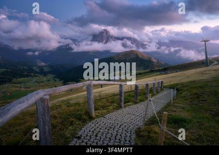 Sentier pavé avec clôture en bois, montagnes dans le brouillard au coucher du soleil Banque D'Images
