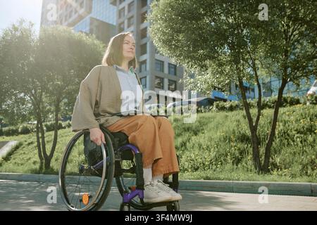 Femme en situation de handicap utilisant un fauteuil roulant dans un parc urbain Banque D'Images