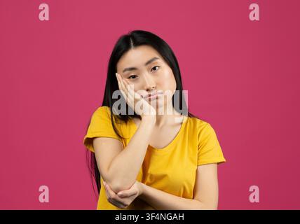 Jeune femme asiatique l'air ennuyé avec la main sur le visage, fond rose Banque D'Images