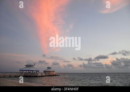 Lever de soleil sur la mer des Caraïbes devant Grand Cayman Island avec des nuages colorés, une eau calme et une jetée au bord de l'eau. Banque D'Images