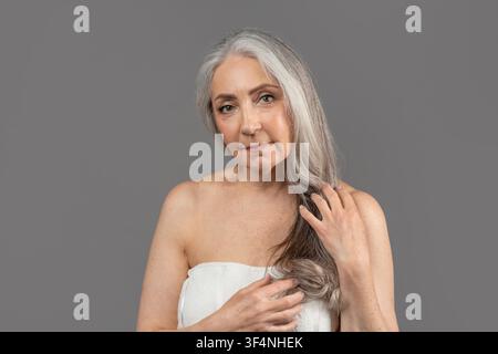 Femme âgée aux cheveux gris tenant des cheveux longs, concept de beauté naturelle Banque D'Images