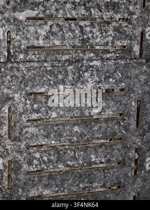Vue rapprochée de panneaux métalliques industriels usés présentant des taches de rouille prononcées, une patine sombre, une texture grise rugueuse et de longues fentes de ventilation horizontales à travers Banque D'Images
