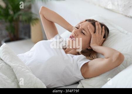 Femme souffrant d'un mal de tête allongée dans le lit, concept de stress et de fatigue Banque D'Images