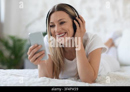 Jeune femme souriante écoutant de la musique avec des écouteurs, se détendant à la maison Banque D'Images
