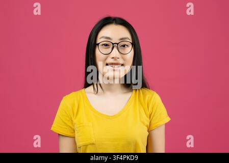 Femme asiatique souriante portant des lunettes devant un fond rose Banque D'Images