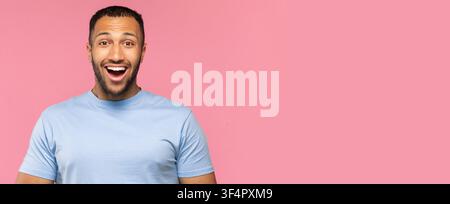Jeune homme souriant avec barbe montrant de l'enthousiasme, fond rose, émotion heureuse Banque D'Images