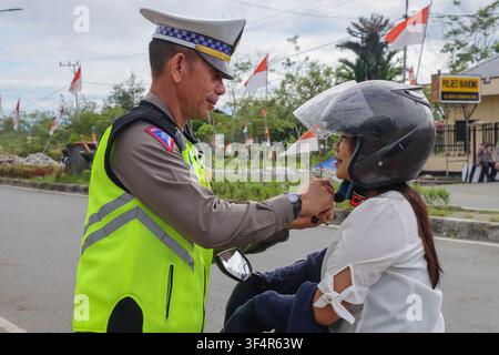 Officier de police routière indonésien aidant une motarde à attacher la sangle de son casque à Yahukimo, Papouasie. Banque D'Images