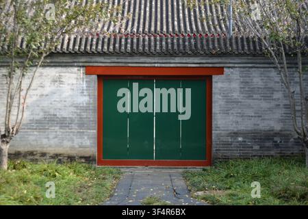 Porte impériale chinoise traditionnelle avec mur de briques gris dans le palais impérial de Pékin, porte en bois à quatre panneaux vert foncé encadrée par un toit au-dessus. Banque D'Images