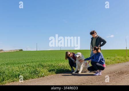 Trois amis souriants caressant un chien de Maremme lors d'une promenade à la campagne Banque D'Images