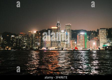 Les gratte-ciel illuminés de la ligne d'horizon de l'île de Hong Kong brillent intensément la nuit le long du Victoria Harbour. Réflexions nocturnes capturées depuis le Star Ferry Banque D'Images