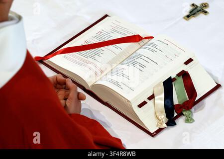 Messe catholique. Un livre liturgique ouvert affiche des textes sacrés, marqués de rubans colorés. Une croix dorée est visible à proximité. Banque D'Images