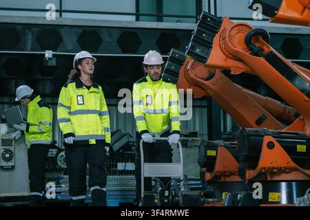 Équipe d'ingénieurs industriels inspectant le stock de bras robotiques dans une usine de fabrication. Concept de service de maintenance de machines industrielles lourdes, équipement qu Banque D'Images