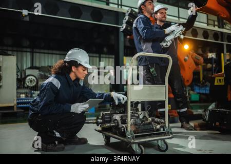 Ingénieure industrielle vérifiant des pièces de machines à bras robotisé à servomoteur électrique pendant que l'équipe d'ingénieurs discute du contrôle des machines à bras robotisé. Con Banque D'Images