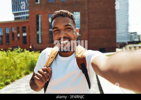 Homme noir souriant prenant un selfie dans un cadre urbain avec un sac à dos, ambiance positive Banque D'Images