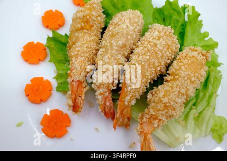 Crevettes tempura enrobées de miettes de pain dorées, disposées sur des feuilles de salade et servies avec des carottes taillées en fleurs. Banque D'Images