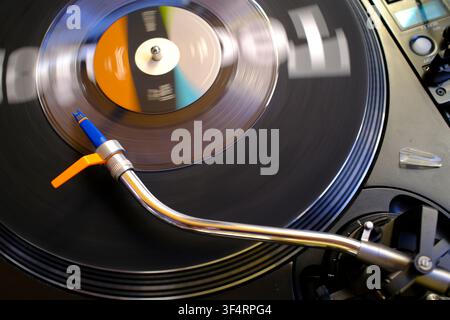 Platine professionnelle en rotation avec un bras tonal argenté, une pointe bleue et un contrepoids orange ; disque en mouvement. Banque D'Images