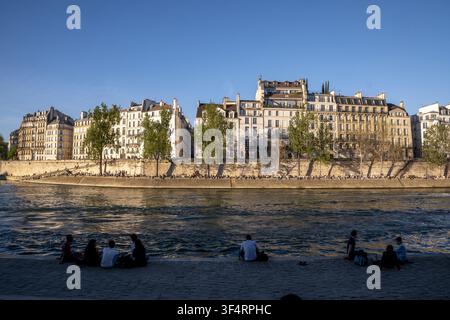 Les rives de la Seine à Paris, en France, prennent vie avec des gens assis et profitant d'une journée ensoleillée, admirant la vue des bâtiments de style Haussmann Banque D'Images