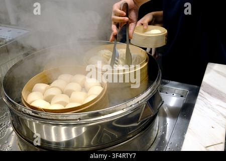 Des petits pains et des boulettes vapeur sont cuits à la vapeur dans des paniers en bambou. Un cuisinier utilise des pinces pour manipuler les aliments. Hoa Lu, Vietnam. Banque D'Images