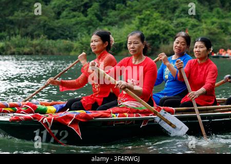 Quatre femmes, vêtues de tenues colorées, rament ensemble dans un bateau traditionnel sur l'eau. Cette scène capture un moment de la vie quotidienne et du travail Banque D'Images