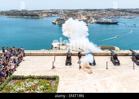 Valletta, Malte – 20 mai 2025 : Les touristes regardent la batterie historique de Saluting Battery tirer un salut de canon traditionnel à midi surplombant le Grand Harbour, le Banque D'Images