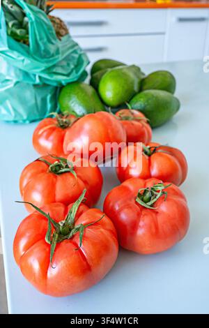 Tomates rouges mûres sur la vigne avec des citrons verts et des avocats sur un comptoir de cuisine Banque D'Images